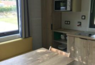 Interieur van een tiny house met eettafel, stoelen en kitchenette bij Flower Camping de la Trye.