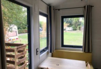 View from a Tiny House with large windows and simple furnishings at Flower Camping de la Trye, France.