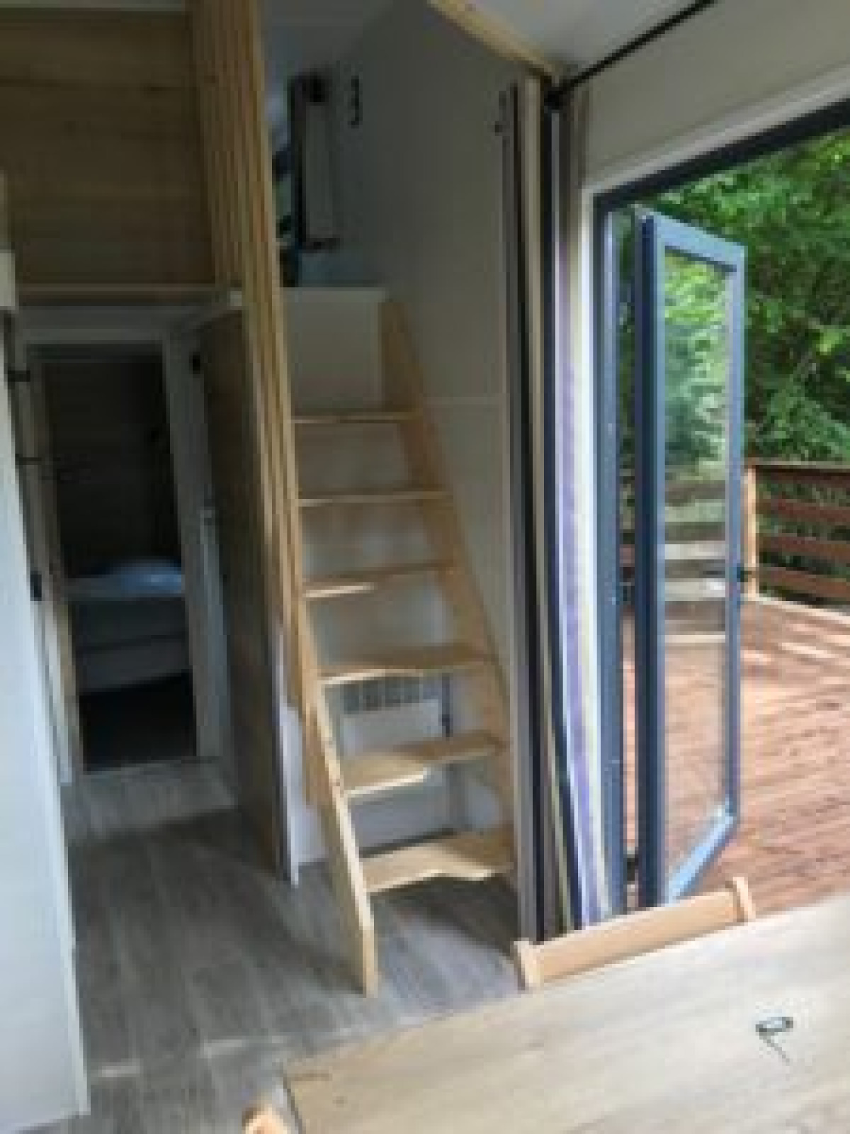 Interieur van Tiny House met houten trap, openstaande deuren naar het terras en boszicht in Frankrijk.