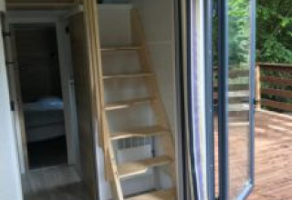 Interieur van Tiny House met houten trap, openstaande deuren naar het terras en boszicht in Frankrijk.