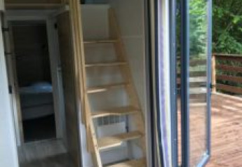Vue intérieure du Tiny House avec escalier en bois, portes ouvertes sur terrasse et vue sur la forêt en France.