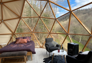 Interno della Dôme Lodge al campeggio Moulin de Chaules in Francia con letto, sedie e vista panoramica.