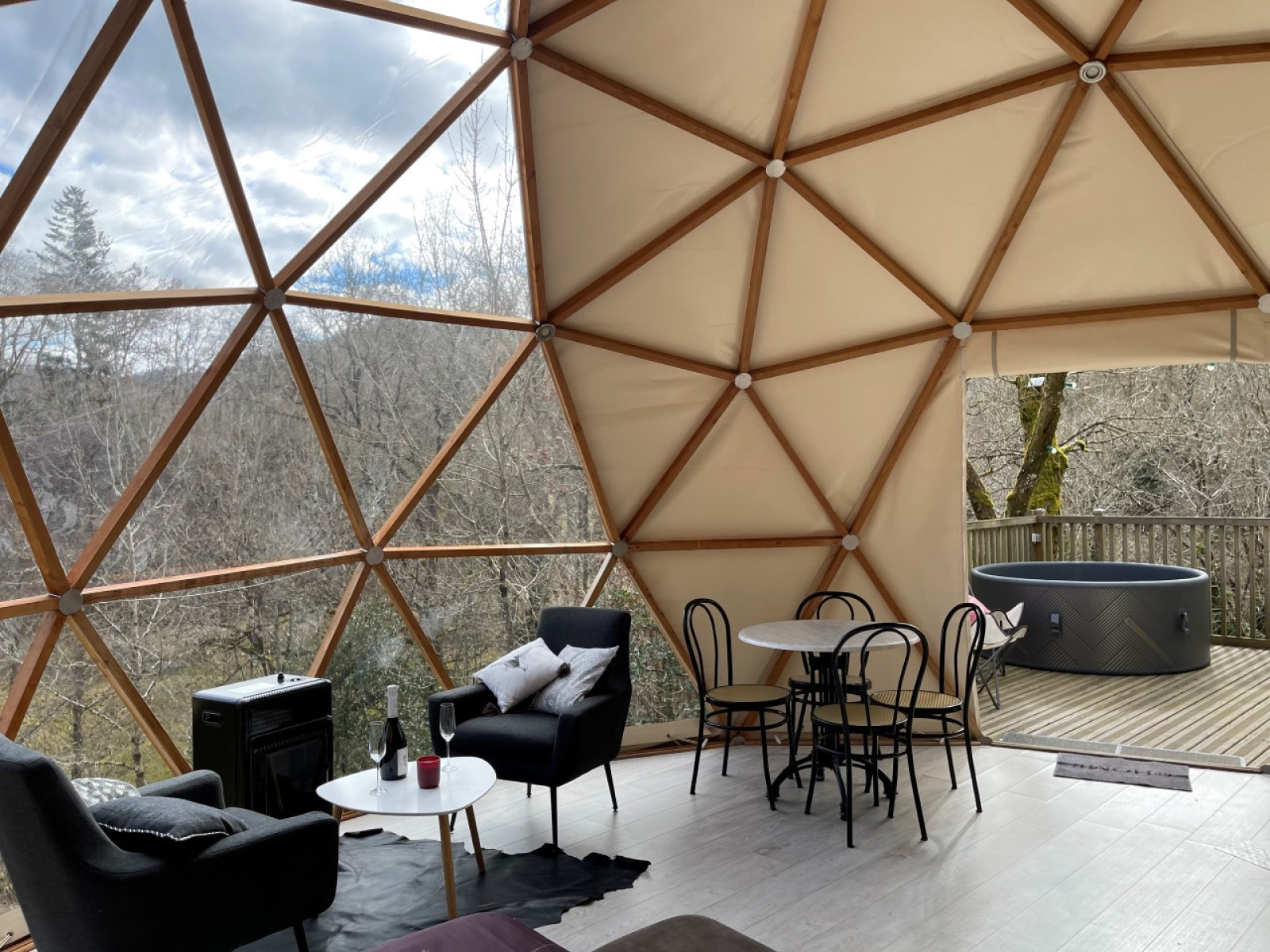 Interieur van de Dôme Lodge op Camping Moulin de Chaules, met koepelramen, zithoek en bubbelbad buiten.