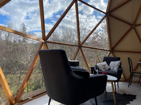 Interior del Dôme Lodge en el camping Moulin de Chaules, Francia, con vista al bosque a través de la cúpula.