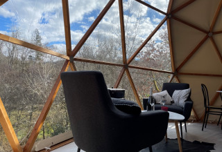 Interior del Dôme Lodge en el camping Moulin de Chaules, Francia, con vista al bosque a través de la cúpula.