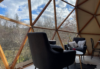Interiør af Dôme Lodge ved Camping Moulin de Chaules, med udsigt over skoven gennem et stort kuppelvindue.