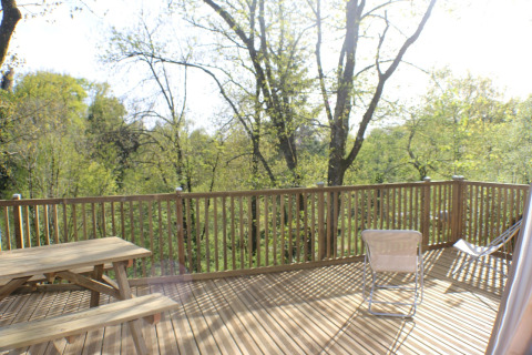 Terrazza in legno con tavolo e sedie al Dôme Lodge, Campeggio Moulin de Chaules, circondata da alberi verdi.