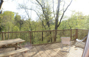 Terrazza in legno con tavolo e sedie al Dôme Lodge, Campeggio Moulin de Chaules, circondata da alberi verdi.