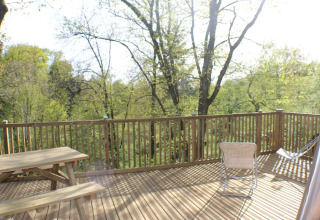 Wooden deck with picnic table and chairs at Dôme Lodge, Campsite Moulin de Chaules, surrounded by trees.