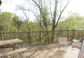 Terrazza in legno con tavolo e sedie al Dôme Lodge, Campeggio Moulin de Chaules, circondata da alberi verdi.