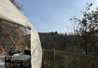 Vista dalla Dôme Lodge al campeggio Moulin de Chaules, con cupola, tavolo e panorama boschivo.