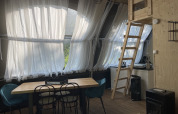 Interior of Lodge 'Big Oak XXL' at Campsite Moulin de Chaules, featuring dining table, ladder, and kitchen.