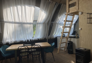 Interno della tenda Lodge 'Big Oak XXL' al Moulin de Chaules con tavolo da pranzo, scala e cucina.