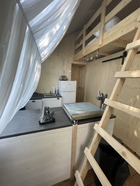 Interno del Lodge «Big Oak XXL» al Moulin de Chaules, Francia, con letto soppalcato e angolo cottura.