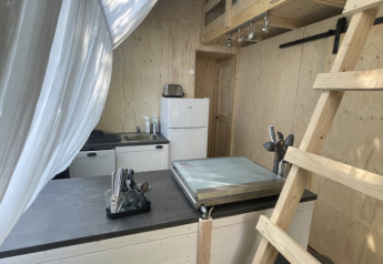 Interno del Lodge «Big Oak XXL» al Moulin de Chaules, Francia, con letto soppalcato e angolo cottura.