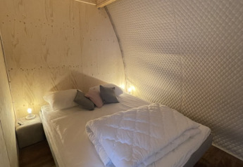 Dormitorio acogedor en la tienda safari Lodge Big Oak XXL en el camping Moulin de Chaules, con paredes de madera.
