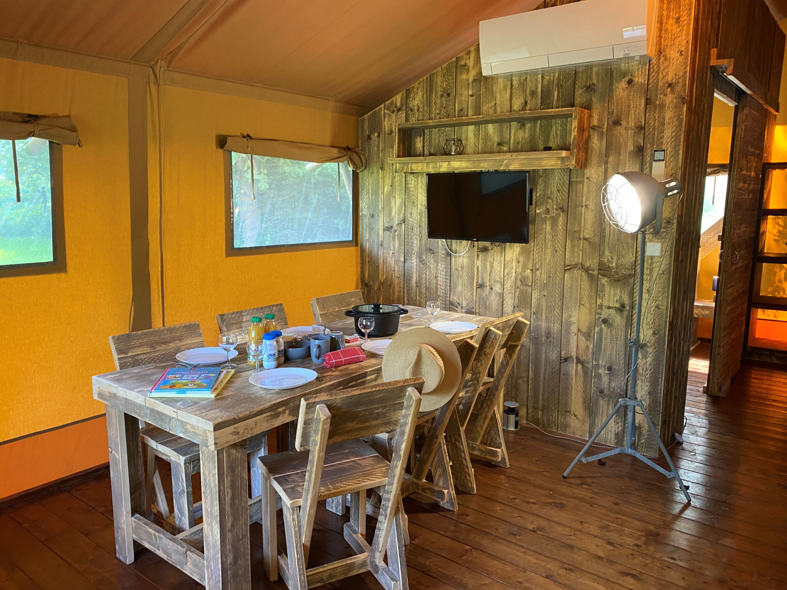 Binnenaanzicht van de Woody Safari Tent met houten meubels, eettafel en TV bij Flower Camping de la Trye in Frankrijk.