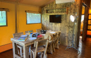 Binnenaanzicht van de Woody Safari Tent met houten meubels, eettafel en TV bij Flower Camping de la Trye in Frankrijk.