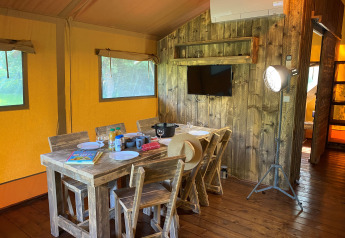 Binnenzicht van de Woody Safari Tent met houten eettafel en TV bij Flower Camping de la Trye in Frankrijk.