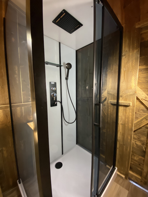 Moderne douche met glazen deuren en regendouche in Woody Safari Tent met jacuzzi bij Flower Camping de la Trye.