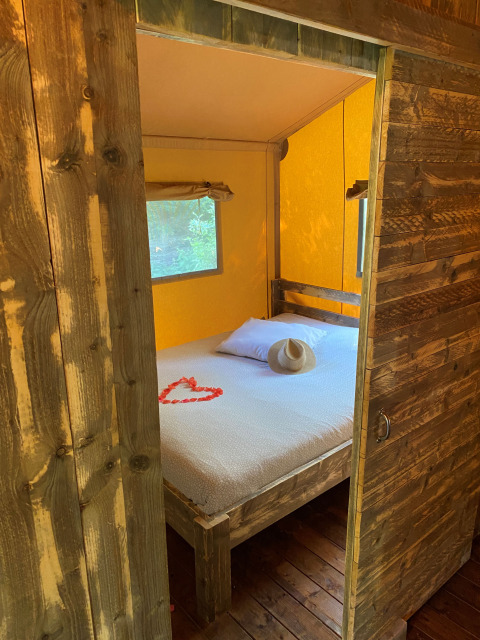 Interieur van Woody Safari Tent met wit bed, houten meubels, hoed en hart van rode bloemblaadjes.