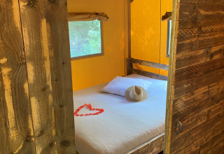 Interieur van Woody Safari Tent met wit bed, houten meubels, hoed en hart van rode bloemblaadjes.