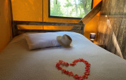 Safari-tent in Frankrijk met een houten bed, hart van bloemblaadjes en hoed op het witte kussen.