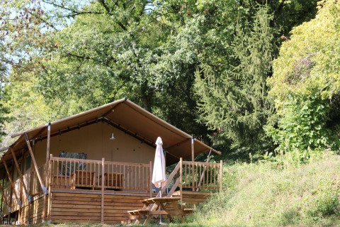 Safari Lodge XL tent at Campsite Moulin de Chaules in France, wooden deck and bench surrounded by trees.