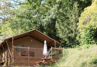 Tenda Safari Lodge XL al campeggio Moulin de Chaules in Francia, veranda in legno circondata dal verde.
