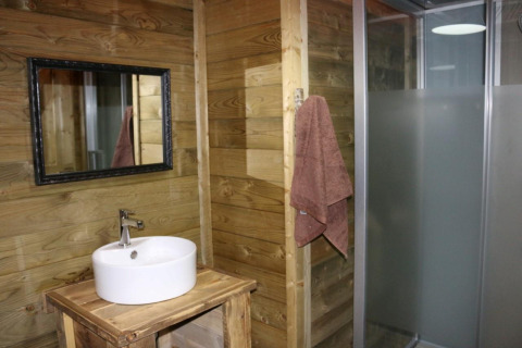 Bagno con pareti in legno, lavabo rotondo, specchio e doccia nella Safari Lodge XL, Moulin de Chaules, Francia.