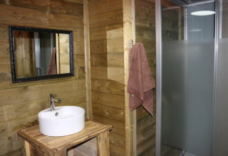 Bagno con pareti in legno, lavabo rotondo, specchio e doccia nella Safari Lodge XL, Moulin de Chaules, Francia.