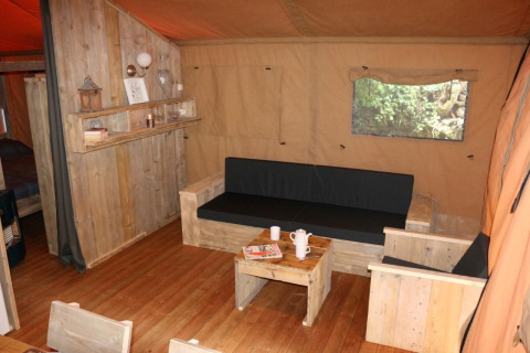 Accogliente soggiorno nella tenda Safari Lodge XL al campeggio Moulin de Chaules in Francia, arredi in legno.