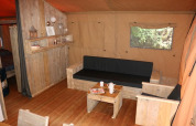 Cozy living area inside Safari Lodge XL tent at Campsite Moulin de Chaules, France, with wooden furniture.