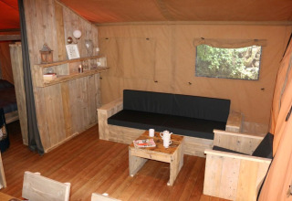 Accogliente soggiorno nella tenda Safari Lodge XL al campeggio Moulin de Chaules in Francia, arredi in legno.