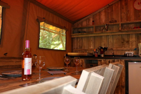 Intérieur du Safari Lodge XL au camping Moulin de Chaules, France, avec table dressée et bouteille de vin.