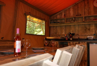 Intérieur du Safari Lodge XL au camping Moulin de Chaules, France, avec table dressée et bouteille de vin.