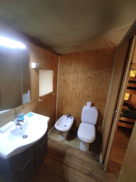 Badezimmer in einem Safarizelt im Centro Vacanze San Marino mit Holzverkleidung, Waschbecken, WC und Bidet.