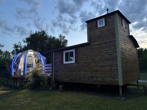 Houten tiny house met verlichte koepel-jacuzzi bij Flower Camping de la Trye in Frankrijk bij schemering.