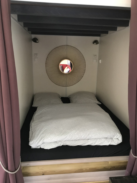 Kleine gezellige slaapnis met tweepersoonsbed en ronde spiegel in een tiny house bij Flower Camping de la Trye.