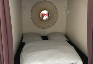 Kleine gezellige slaapnis met tweepersoonsbed en ronde spiegel in een tiny house bij Flower Camping de la Trye.