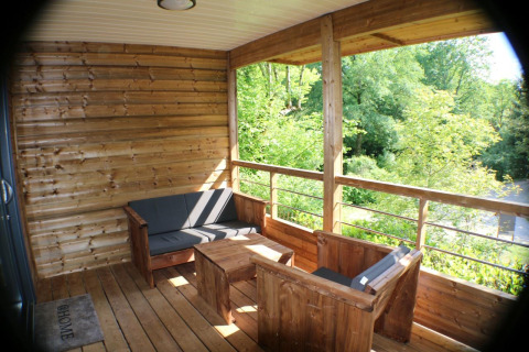 Terraza de madera con asientos y vistas al bosque en cabaña de Campsite Moulin de Chaules, Francia.