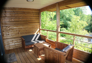 Terraza de madera con asientos y vistas al bosque en cabaña de Campsite Moulin de Chaules, Francia.