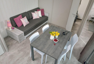 Gemütliches Wohnzimmer im Holzchalet am Campingplatz Moulin de Chaules mit Sofa, Esstisch und Blumen.