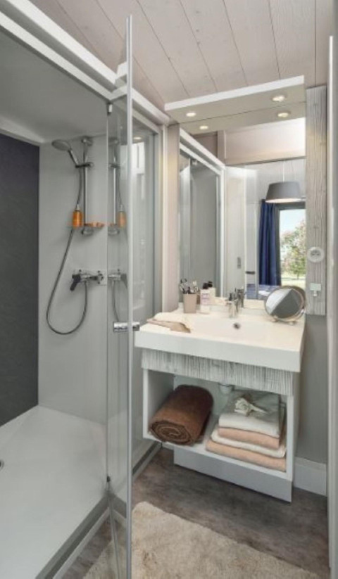 Baño moderno con ducha, lavabo, espejo y toallas en un chalet de madera en Moulin de Chaules, Francia.