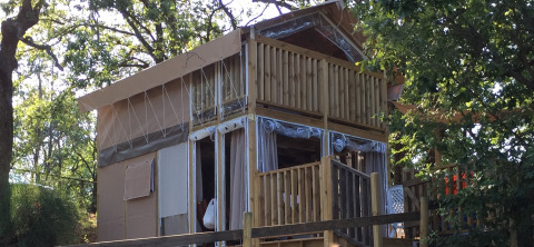 La tenda safari Air Lodge è mostrata tra gli alberi, con veranda in legno e ampie finestre immerse nella natura.