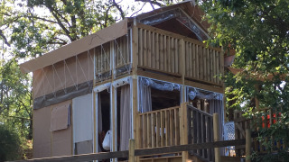 La tenda safari Air Lodge è mostrata tra gli alberi, con veranda in legno e ampie finestre immerse nella natura.