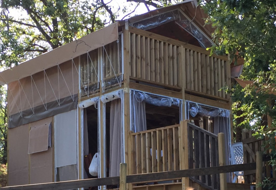 De Air Lodge safaritent staat tussen de bomen, met houten veranda en grote ramen met uitzicht op de natuur.