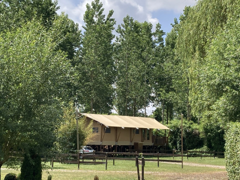 Gran tienda safari con porche cubierto en Flower Camping de la Trye, rodeada de árboles verdes en Francia.