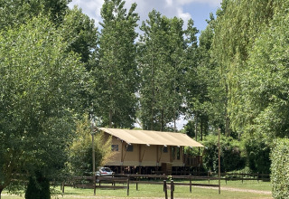 Grote safaritent met overdekte veranda op Flower Camping de la Trye, omgeven door groen in Frankrijk.