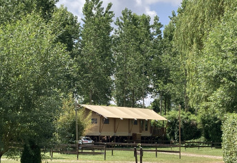 Large safari tent with covered porch at Flower Camping de la Trye, surrounded by greenery and tall trees in France.